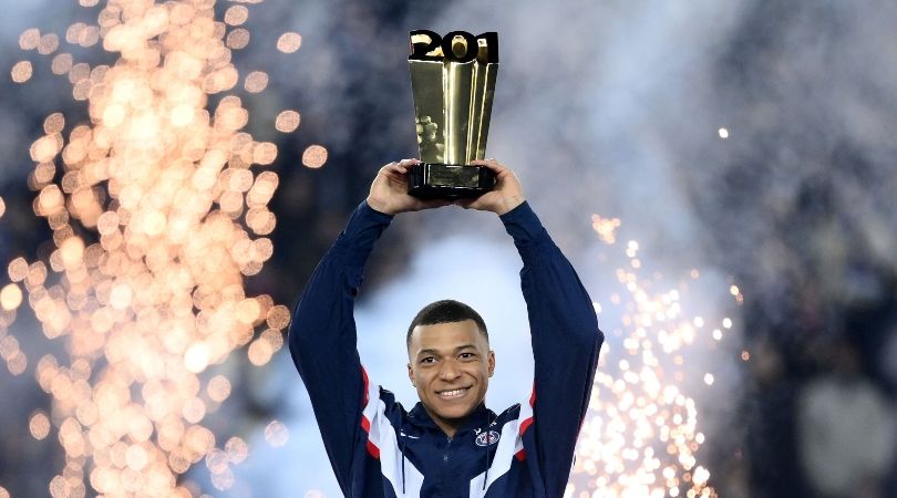 Kylian Mbappe holds a trophy aloft in a ceremony after PSG