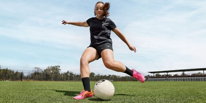 A female footballer wearing Asics football boots striking a ball