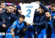 Greece players hold up a shirt bearing George Baldock's name and number two after their victory against England