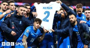 Greece players hold up a shirt bearing George Baldock's name and number two after their victory against England