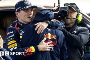 Max Verstappen embraces a Red Bull team member after winning the F1 world title, with a TV cameraman in the background