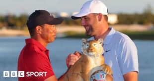 Host Tiger Woods shakes hands with winner Scottie Scheffler at the 2024 Hero World Challenge event, beside the tournament trophy