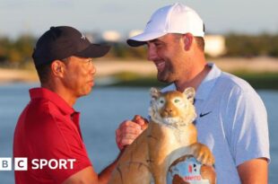 Host Tiger Woods shakes hands with winner Scottie Scheffler at the 2024 Hero World Challenge event, beside the tournament trophy